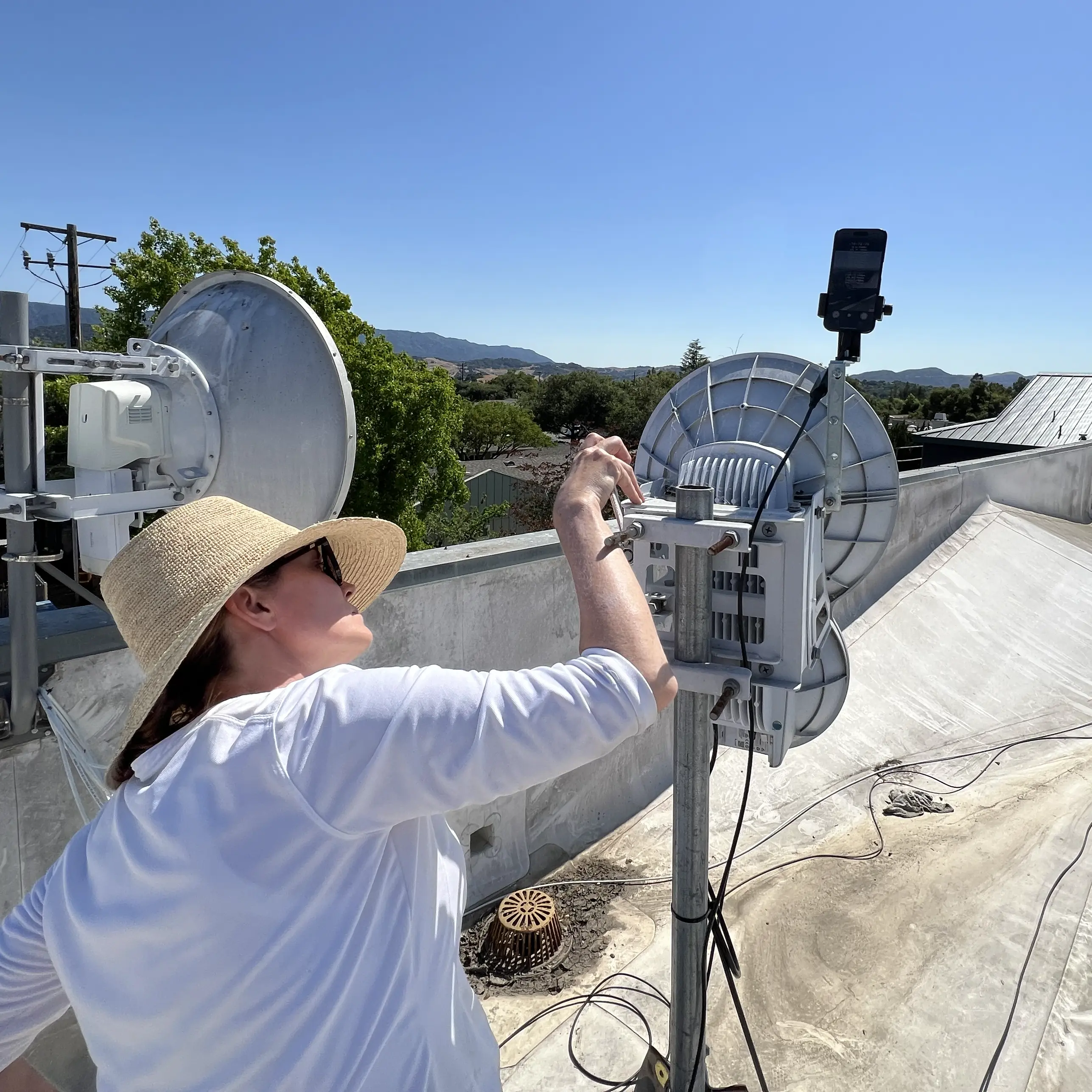 Technician sweeping AirFiber 24 with iPhone mounted on L-bracket, rooftop alignment in progress
